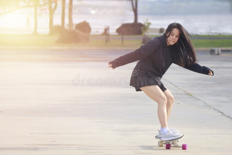 Asian women on skates board outdoors on beautiful summer day. Happy young women play surfskate at park on morning time. Sport