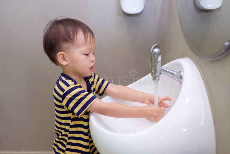 Asian 2 years old toddler baby boy child washing hands by himself on white sink and water drop from faucet in public toilet