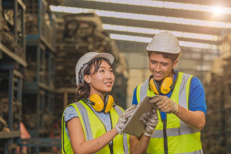 Asian young man and women worker team engineer working help support together using tablet happy smile to work in factory industry royalty free stock photo