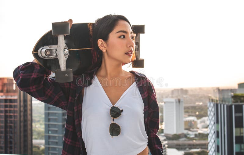 Asian young women surf skate or skates board outdoors on beautiful summer day. Happy young women play surf skate at roof top