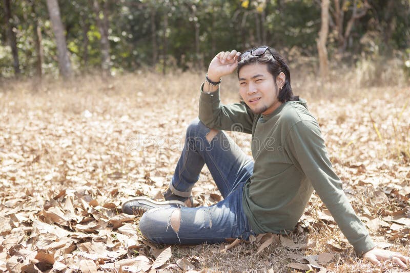 Asian younger man sitting on dry leaves field with smiling face