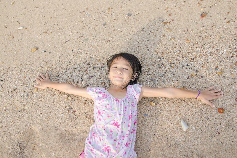Asiat som ler den gulliga lilla flickan som ligger på strandsanden Thailändsk chi royaltyfri foto Asiat som ler den gulliga lilla flickan som ligger på strandsanden Thailändsk chi royaltyfri foto
