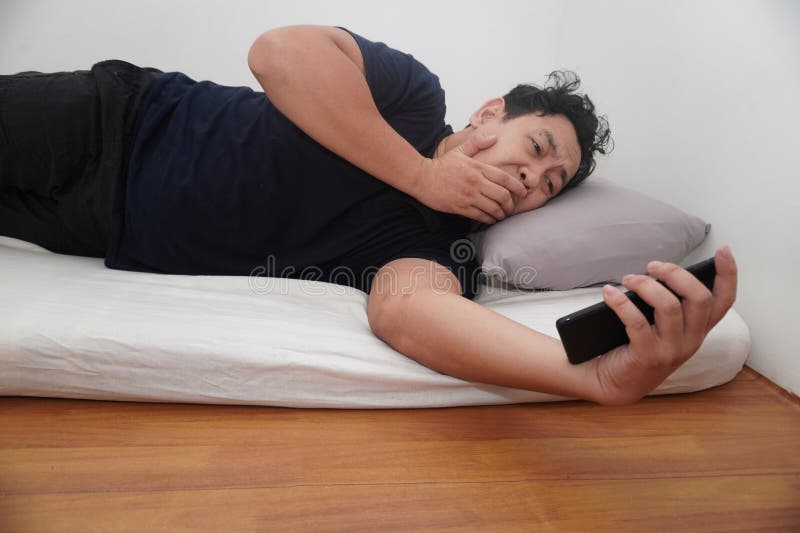 Asiatico controlla il telefono subito dopo essersi svegliato a letto la mattina fotografia stock libera da diritti