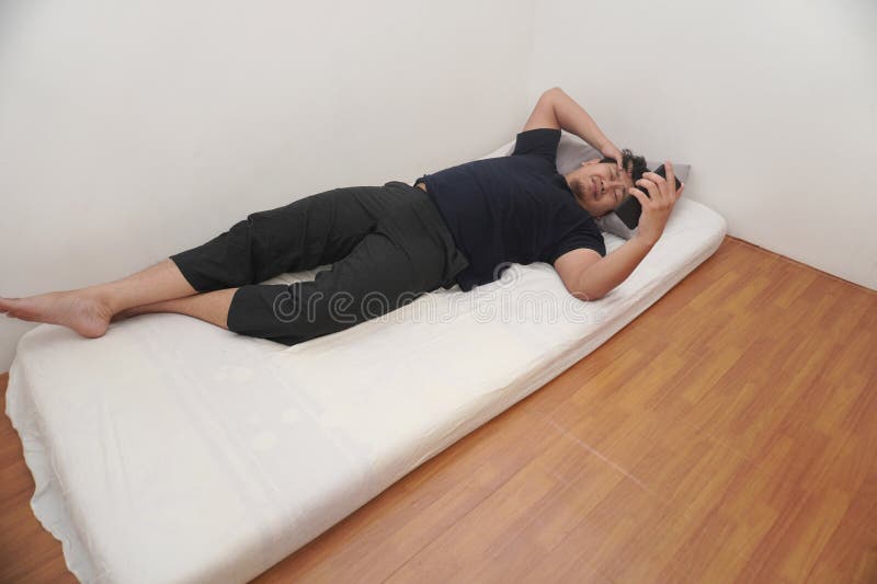 Asiatico controlla il telefono subito dopo essersi svegliato a letto la mattina fotografie stock