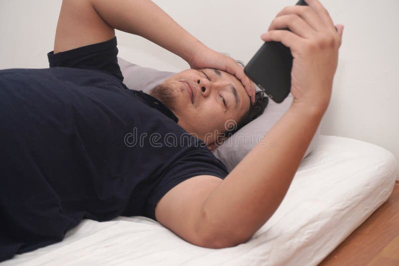 Asiatico controlla il telefono subito dopo essersi svegliato a letto la mattina immagini stock