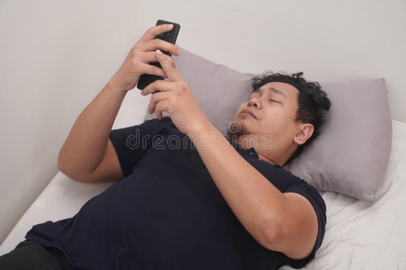 Asiatico controlla il telefono subito dopo essersi svegliato a letto la mattina fotografia stock