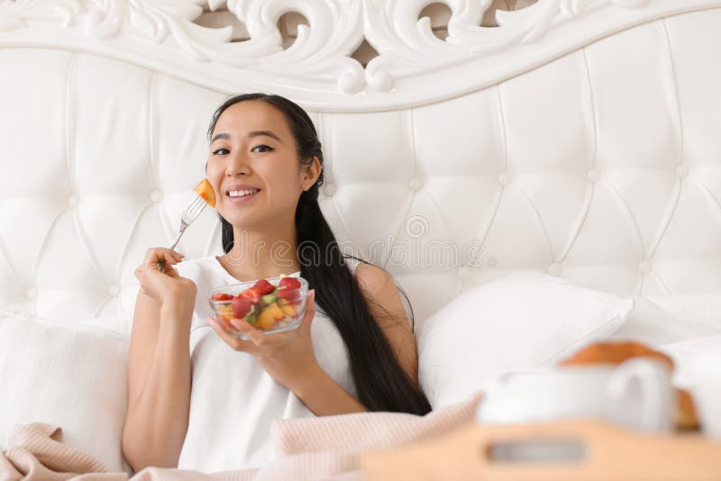 Asiatin, die zu Hause gesunden Obstsalat zum Frühstück isst stockfotografie Asiatin, die zu Hause gesunden Obstsalat zum Frühstück isst stockfotografie