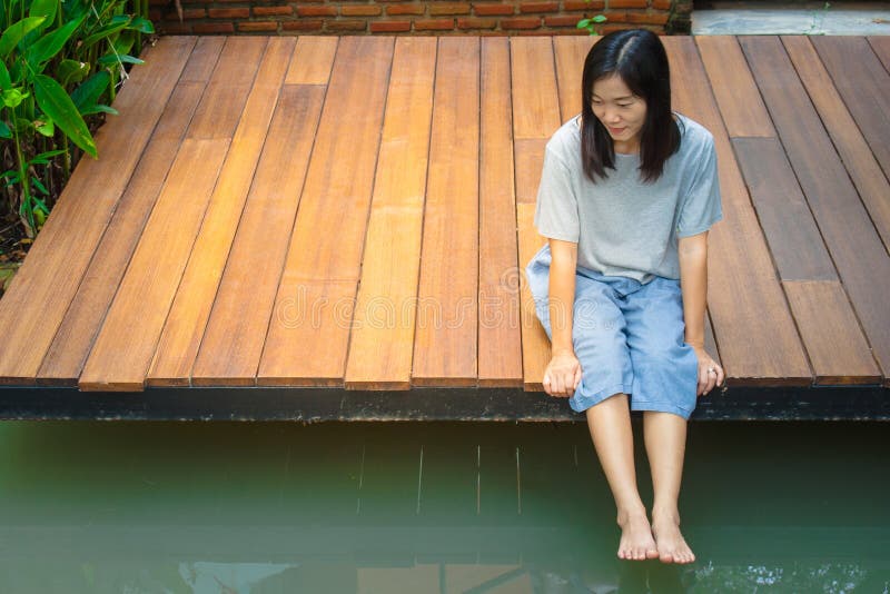 Asiatinsitzen entspannen sich auf hölzerner Terrasse oder Portal nahe Teich im Garten lizenzfreies stockbild Asiatinsitzen entspannen sich auf hölzerner Terrasse oder Portal nahe Teich im Garten lizenzfreies stockbild