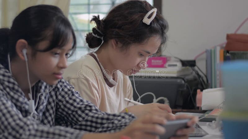 Asiatique jolie adolescente apprendre leçon en ligne avec tablette numérique sur le bureau pendant que sa soeur aime jouer à des j banque de vidéos