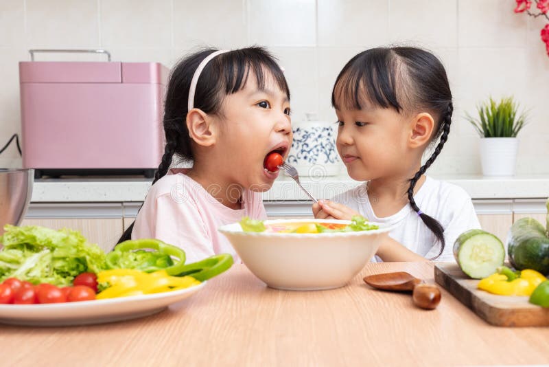 Asiatische chinesische kleine Schwestern, die zu Hause Salat in der Küche machen stockfotografie Asiatische chinesische kleine Schwestern, die zu Hause Salat in der Küche machen stockfotografie
