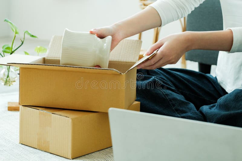 Asiatische Eigentümerin, die ein Produkt zusammenpackt und in einem Pappkarton verpackt. Asiatische Unternehmerin packt Produkte in Kartons mit Kunden. Ideen für Online-Geschäfte und Freelance.