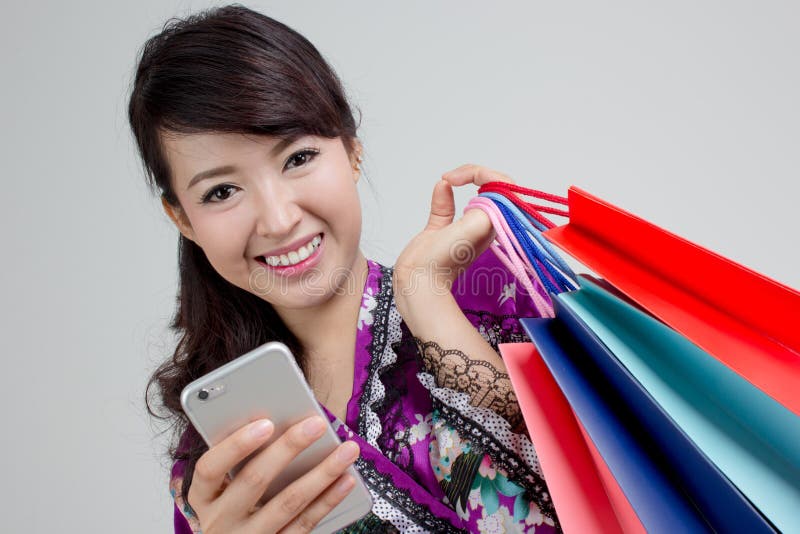 Asiatische Einkaufsfrau, die intelligentes Telefon verwendet und bunte Einkaufstaschen hält lizenzfreie stockfotos Asiatische Einkaufsfrau, die intelligentes Telefon verwendet und bunte Einkaufstaschen hält lizenzfreie stockfotos