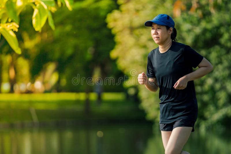 Asiatische Frau von mittlerem Alter, die ein schwarzes Kleid, blauen Hut, laufendes in Park zum See nahe ausdehnen tr?gt Erhalten stockfotografie Asiatische Frau von mittlerem Alter, die ein schwarzes Kleid, blauen Hut, laufendes in Park zum See nahe ausdehnen tr?gt Erhalten stockfotografie