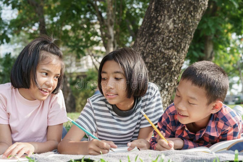 Asiatische Grundschulkinder der Fraktion schreiben ein Notebook mit einem Stift und gemeinsam am Morgen lernen in den Sommer am P stockfotos