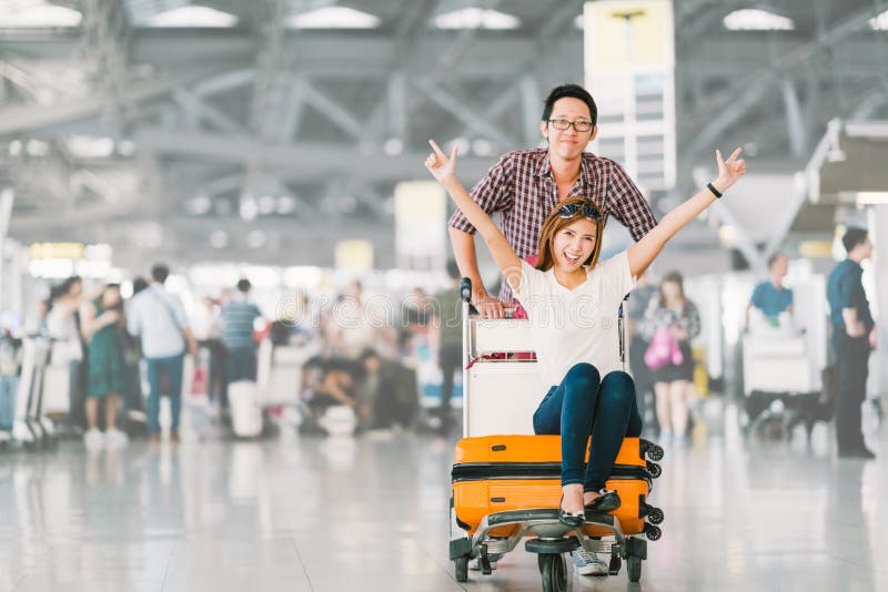 Young Asian tourist couple happy and excited together for the trip, girlfriend sitting and cheering on baggage trolley or luggage cart. Holiday vacation travelling abroad concept, with copy space. Young Asian tourist couple happy and excited together for the trip, girlfriend sitting and cheering on baggage trolley or luggage cart. Holiday vacation travelling abroad concept, with copy space