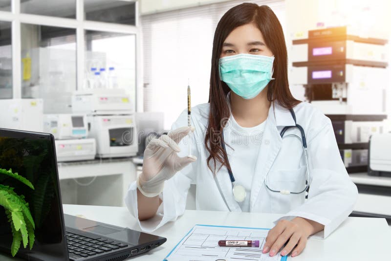 Asiatischer Arzt hält ein Spritzenblutbeispielreagenzglas für covid19 Analyse mit Patientenakte auf Schreibtisch im Labor. Laboran