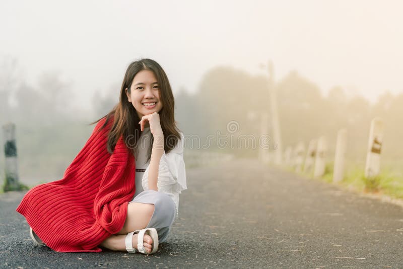 Asiatischer Jugendlicher, der eine rote Strickjacke morgens sitzt mitten in der Stra?e durch den Nebel des Reservoirs tr?gt lizenzfreie stockbilder Asiatischer Jugendlicher, der eine rote Strickjacke morgens sitzt mitten in der Stra?e durch den Nebel des Reservoirs tr?gt lizenzfreie stockbilder