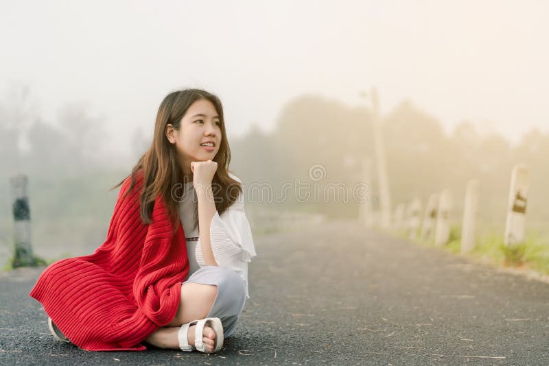 Asiatischer Jugendlicher, der eine rote Strickjacke morgens sitzt mitten in der Stra?e durch den Nebel des Reservoirs tr?gt lizenzfreie stockfotografie Asiatischer Jugendlicher, der eine rote Strickjacke morgens sitzt mitten in der Stra?e durch den Nebel des Reservoirs tr?gt lizenzfreie stockfotografie