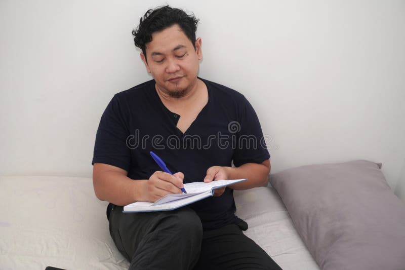 Asiatischer Erwachsener, der täglich Tagebuch über sein Bett schreibt, um sein Leben zu reflektieren