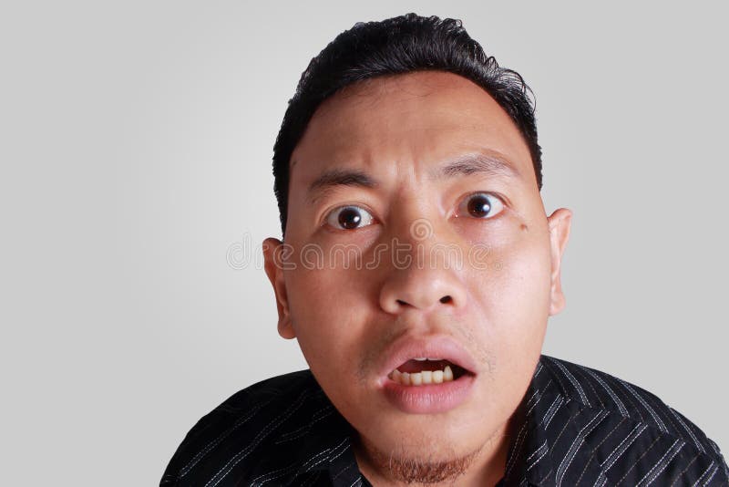 Headshot portrait of young funny Asian man shocked surprised or terrified expression with mouth open, isolated on grey. Headshot portrait of young funny Asian man shocked surprised or terrified expression with mouth open, isolated on grey