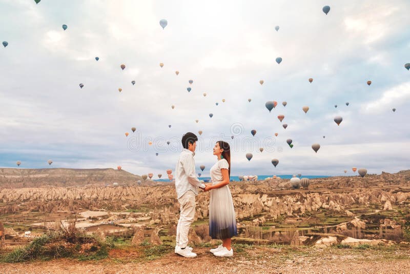 Asiatisches Ehepaar sieht bunten Heißluftballons über das Tal fliegen in Kappadokien, Türkei Diese romantische Zeit der Liebe lizenzfreie stockfotos Asiatisches Ehepaar sieht bunten Heißluftballons über das Tal fliegen in Kappadokien, Türkei Diese romantische Zeit der Liebe lizenzfreie stockfotos