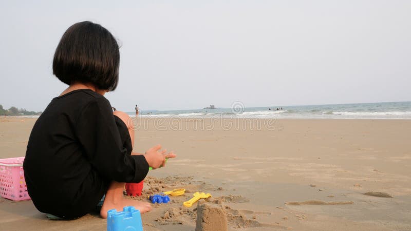 Asiatisches kleines Mädchen, das auf dem Meersandstrand spielt mit, vor der Glättung der Atmosphäre