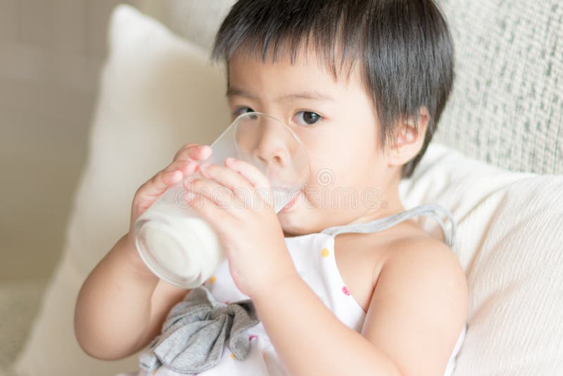Asiatisches kleines Mädchen ist, trinkend halten und ein Glas Milch im liv lizenzfreies stockbild Asiatisches kleines Mädchen ist, trinkend halten und ein Glas Milch im liv lizenzfreies stockbild