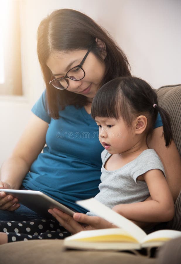 Asiatisches Kleinkind und junges Muttersitzen und Anwendung des digitalen tabl. Asiatisches Kleinkindmädchen und junges Muttersitzen und digitale Tablette zusammen verwenden Wissen und Lernkonzept