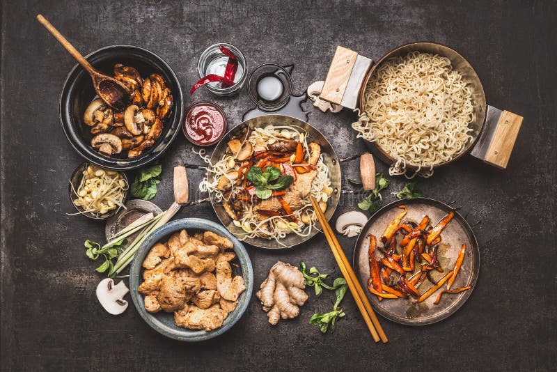 Asiatisches Lebensmittelkochen Wok mit Nudelhühneraufruhrfischrogen und Gemüsebestandteilen mit Gewürzen, Soßen und Essstäbchen a