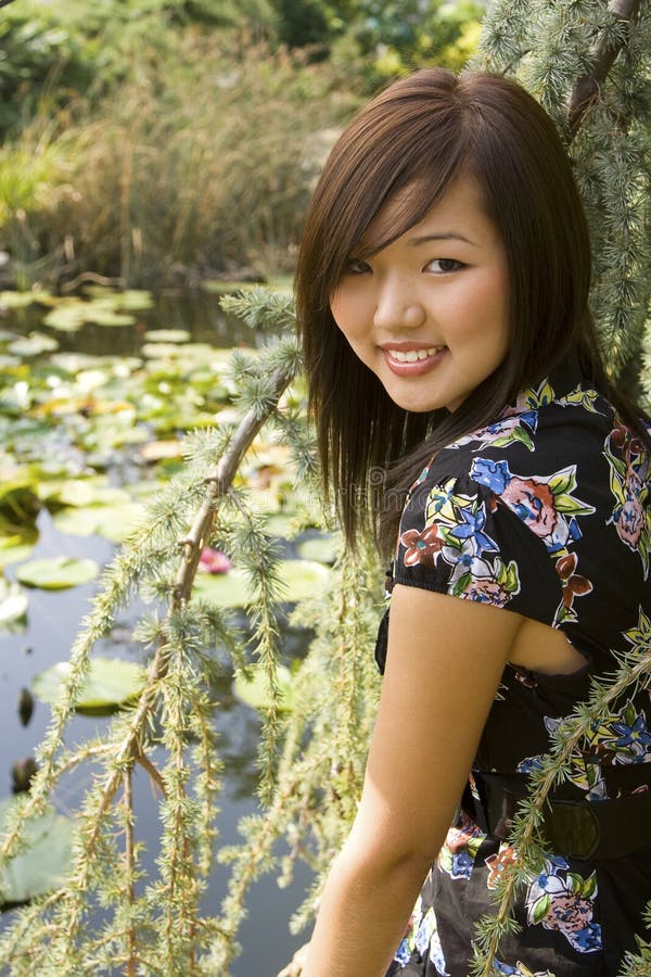 Asiatisches Mädchen des Brunette, das am Seeufer sitzt.