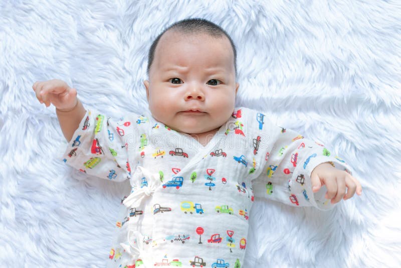 Asiatisches Säuglingsbaby ralaxing auf dem weißen Bett Es passt an mir auf Es ist Gesicht ist Stirnrunzeln lizenzfreies stockbild Asiatisches Säuglingsbaby ralaxing auf dem weißen Bett Es passt an mir auf Es ist Gesicht ist Stirnrunzeln lizenzfreies stockbild