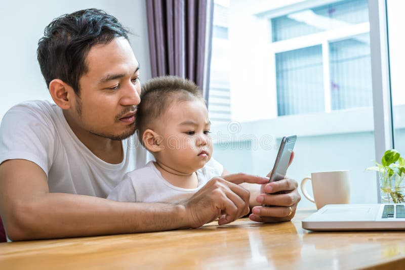 Asiatisk fader och son som tillsammans använder den smarta telefonen i hem- bakgrund Teknologi- och folkbegrepp Livsstilar och ly