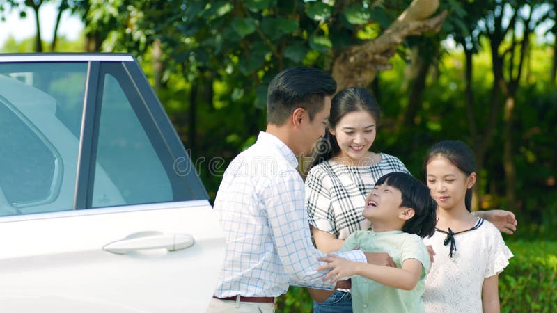 Asiatisk fader som rymmer hans son ut från bilen med modern & dottern beside