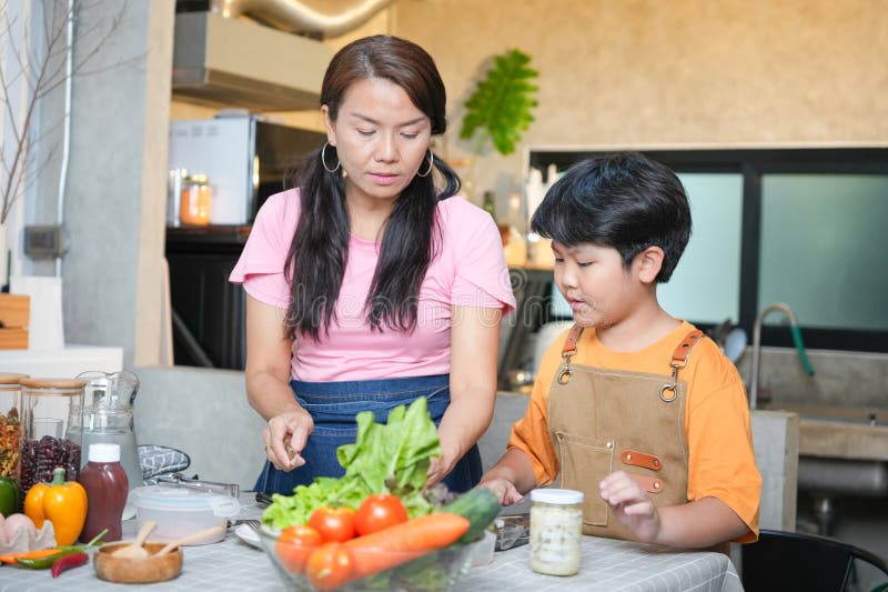 Asiatisk familj som förbereder en hälsosam måltid på hemmoder och son som kokar tillsammans i ett modernt kök och barnundervisning royaltyfri bild