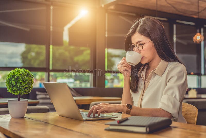 Asiatisk funktionsduglig kvinna som anv? nder b? rbara datorn och dricker kaffe i kaf? Folk och livsstilbegrepp Teknologi- och aff? royaltyfri fotografi
