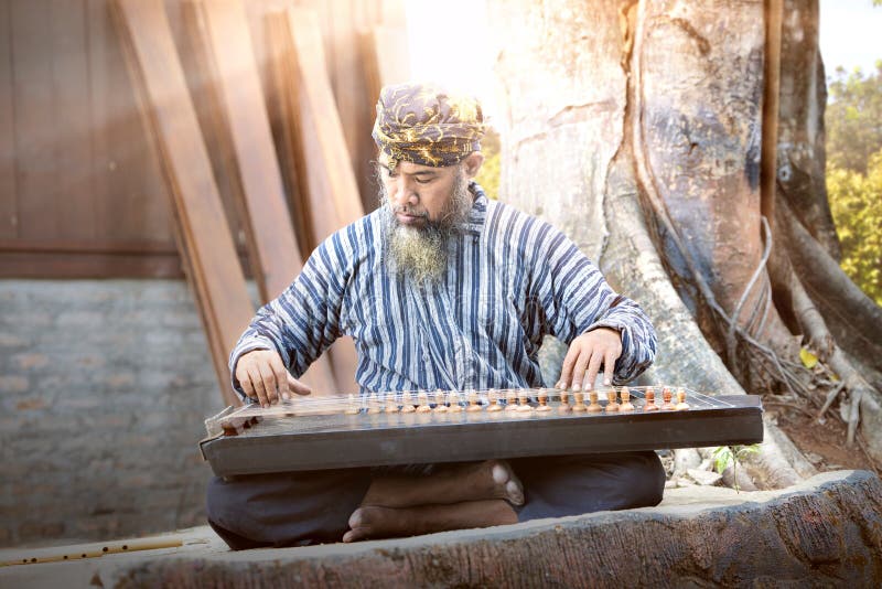 Asiatisk gammal man som spelar kecapi med trädbakgrund arkivbild Asiatisk gammal man som spelar kecapi med trädbakgrund arkivbild