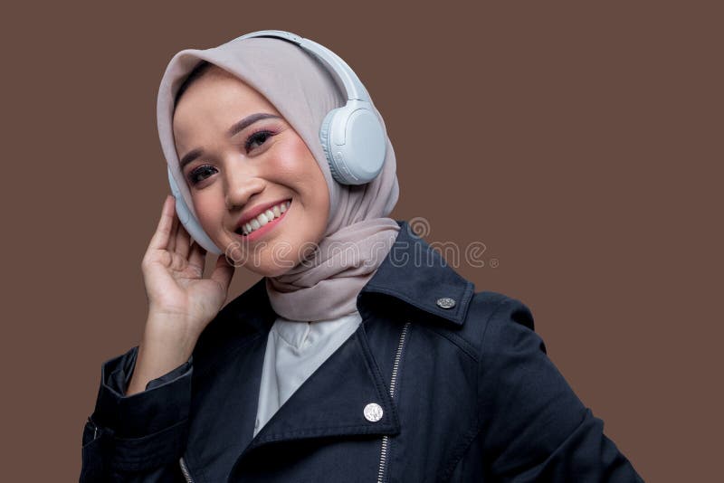Asiatisk hijab-kvinna som bär trådlösa hörlurar med ett leende som tittar på kameran arkivfoton