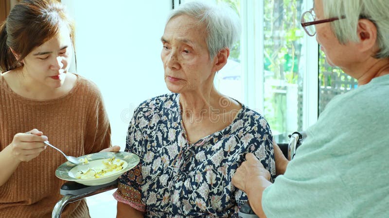 Asiatisk kvinna som ger trötta äldre patienter, anorexi, äter mindre mat, deprimerade äldre kvinnor lider av depression, symtom