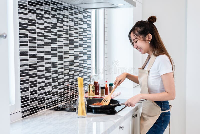 Asiatisk kvinna som lyckligt lagar mat spagetti i kök Folk och livsstilbegrepp Mat- och drinktema Inregarnering och ho