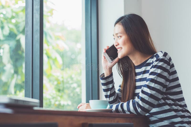 Asiatisk kvinna som talar på mobiltelefonen och sitter på kaférestauraen fotografering för bildbyråer Asiatisk kvinna som talar på mobiltelefonen och sitter på kaférestauraen fotografering för bildbyråer