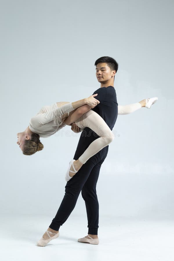 Asiatisk man och kaukasisk kvinna som utför säckdansare på grå i Studio under föreställningar som klassisk dans och Choreografi royaltyfria foton