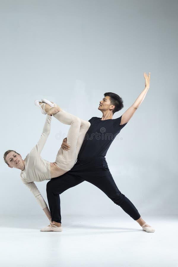 Asiatisk man och kaukasisk kvinna som utför säckdansare på grå i Studio under föreställningar som klassisk dans och Choreografi royaltyfri foto
