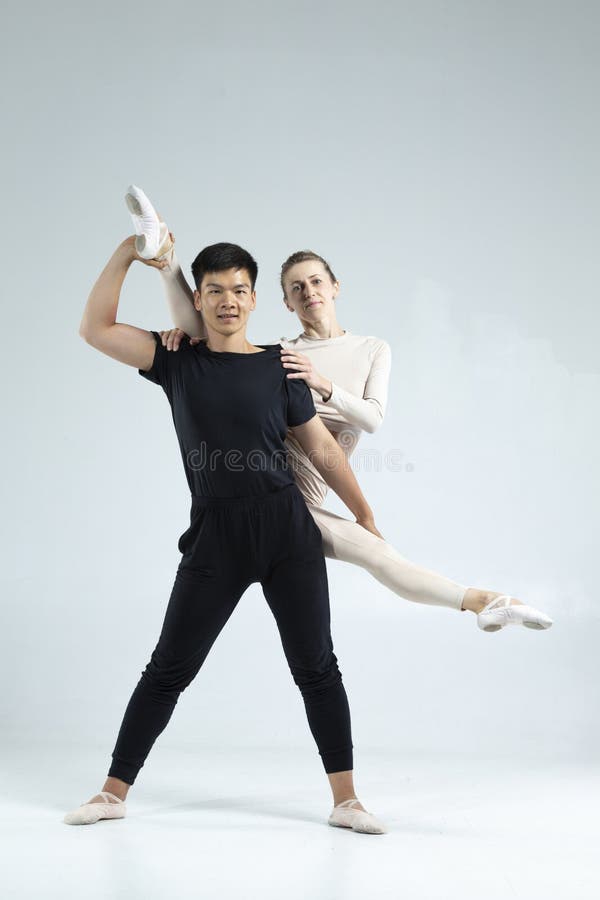 Asiatisk man och kaukasisk kvinna som utför säckdansare på grå i Studio under föreställningar som klassisk dans och Choreografi en royaltyfri foto