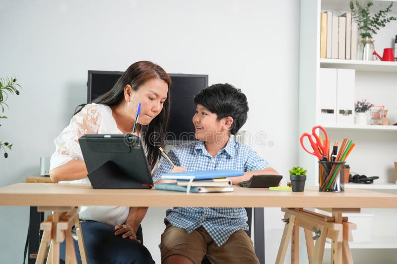 Asiatisk moder Tutoring Son på hemmaplan Helping Young Boy med hemläxor i bostadsrummet royaltyfria bilder