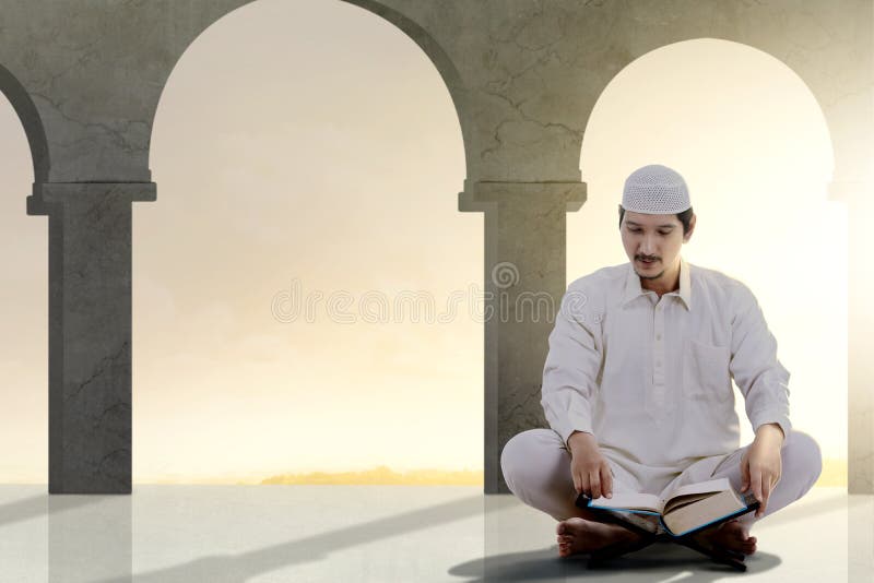 Asiatisk muslimsk man som sitter och att läsa Koranen arkivbild Asiatisk muslimsk man som sitter och att läsa Koranen arkivbild