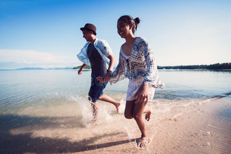 Asiatisk tonårsflicka och pojke som springer på stranden