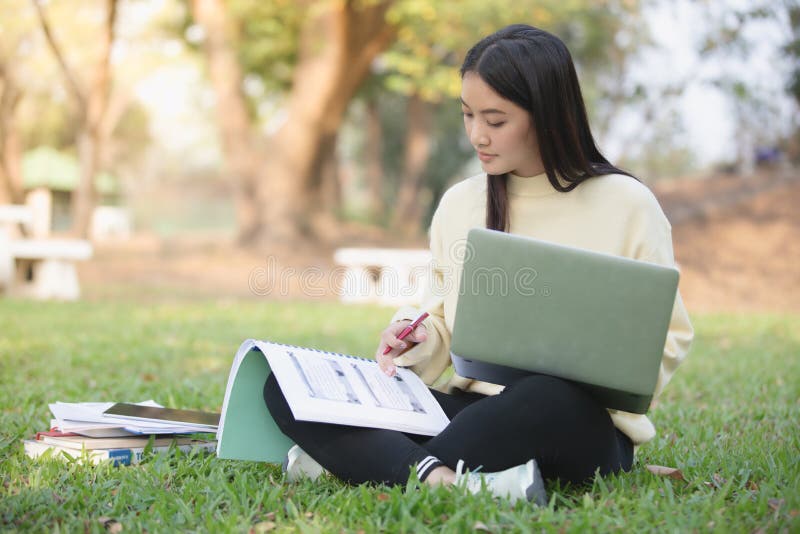 Asiatiska kvinnauniversitetsstudenter som ler och sitter på green royaltyfria bilder Asiatiska kvinnauniversitetsstudenter som ler och sitter på green royaltyfria bilder