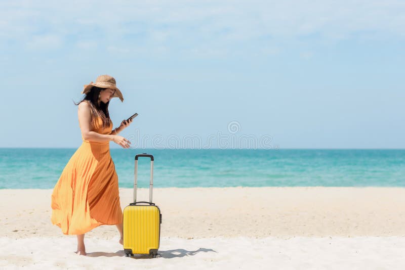 Asiatiska kvinnor som reser med gult bagage går och checkar in smart telefon på stranden Summan av resetjänstresor och turistplan royaltyfria bilder Asiatiska kvinnor som reser med gult bagage går och checkar in smart telefon på stranden Summan av resetjänstresor och turistplan royaltyfria bilder