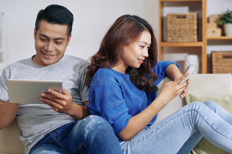 Asiatiska par genom att använda minnestavlan och smartphonen hemma royaltyfria bilder Asiatiska par genom att använda minnestavlan och smartphonen hemma royaltyfria bilder