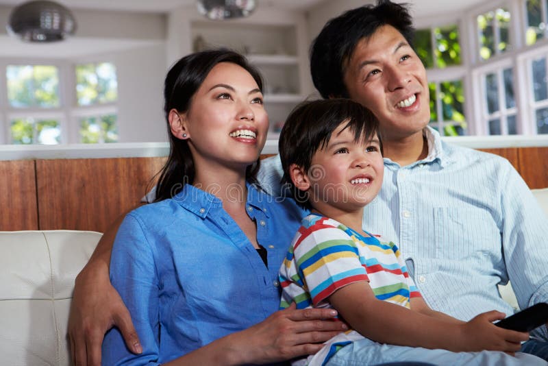 Asiatiskt familjsammanträde på Sofa Watching TV tillsammans arkivbild Asiatiskt familjsammanträde på Sofa Watching TV tillsammans arkivbild